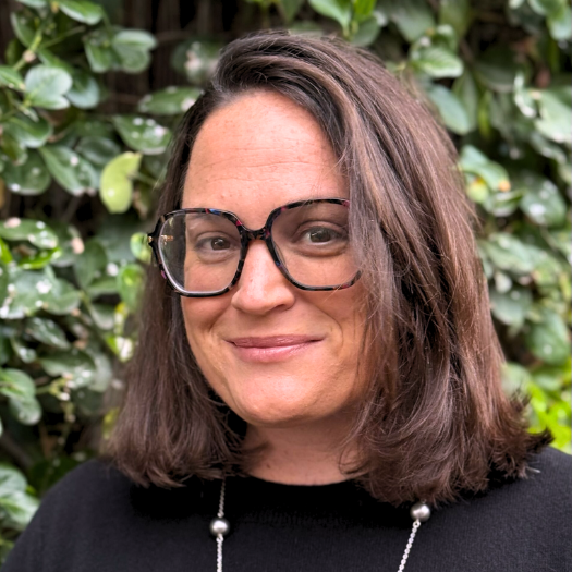 Headshot of Whitney Rubenstein in front of dark green leaves.