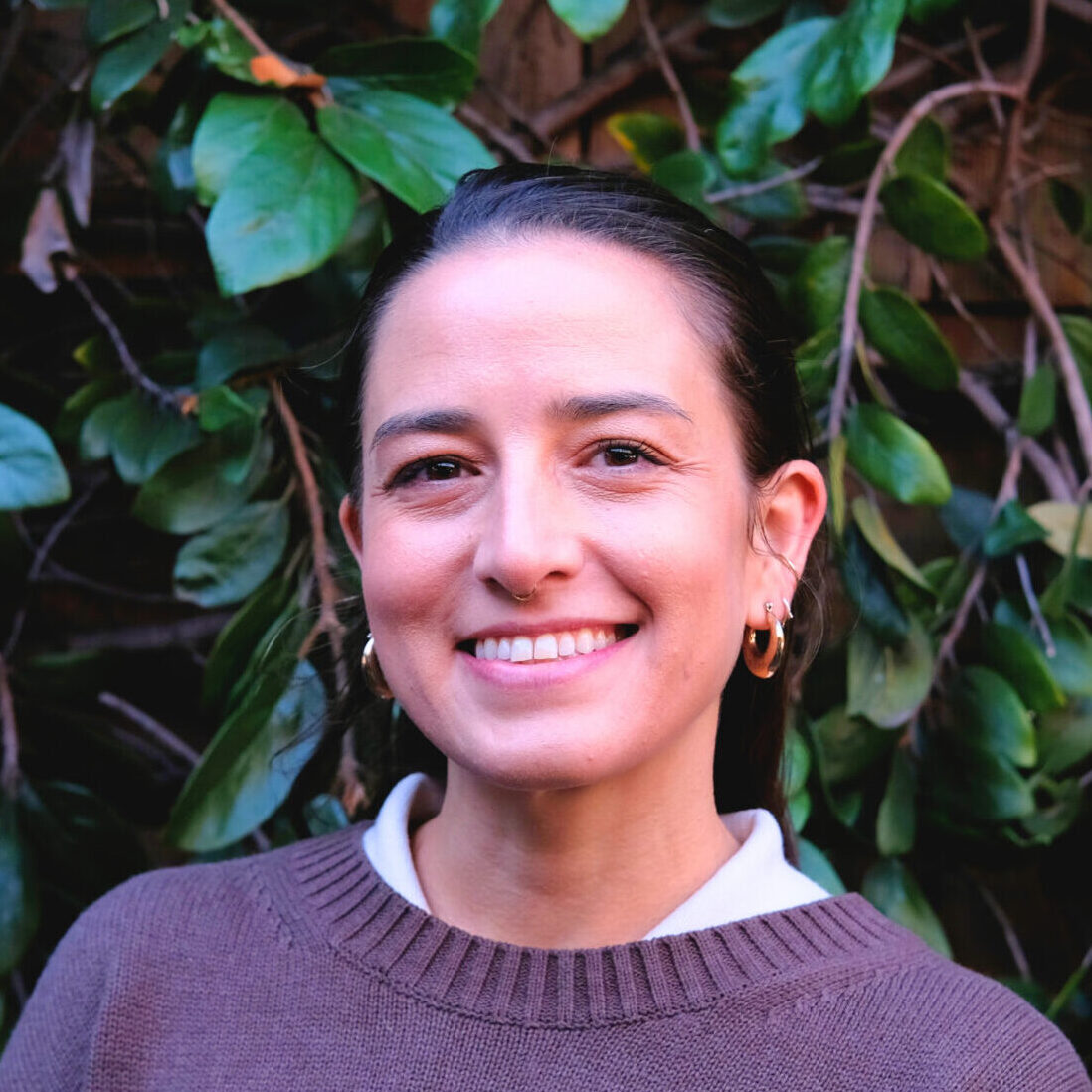 Caitlin Jolicoeur headshot in front of dark green leaves.
