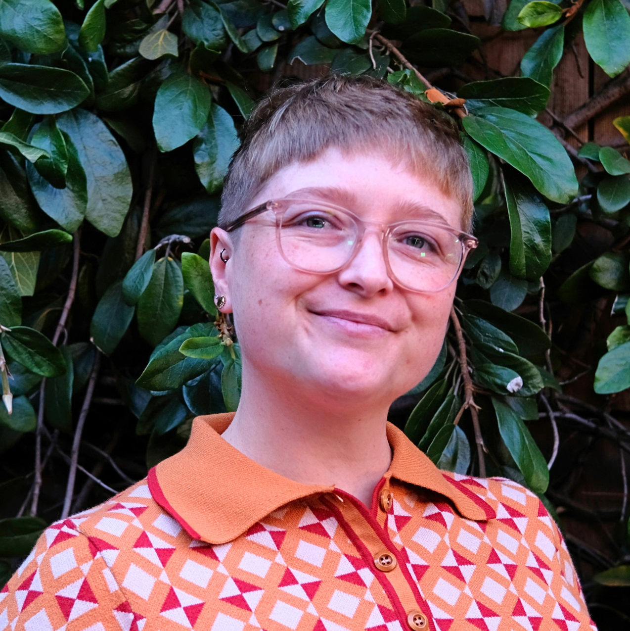 Headshot of Ari Jones in front of a dark green leaf background.