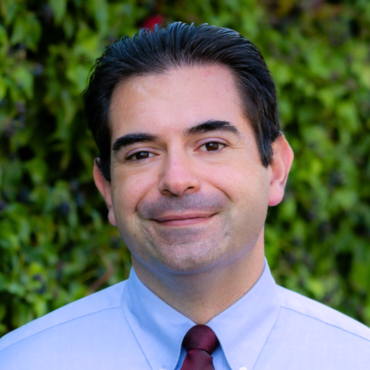 Headshot of Miguel Soto in front of dark green leaves.